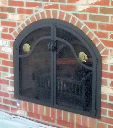 Osterville Arch With Nauset Wave Design Black finish frame and twin door with standard forged handle. Antique brass finish scallop shells, standard forged handles and smoked glass.  No mesh, no draft.   (Installed on raised firebox)